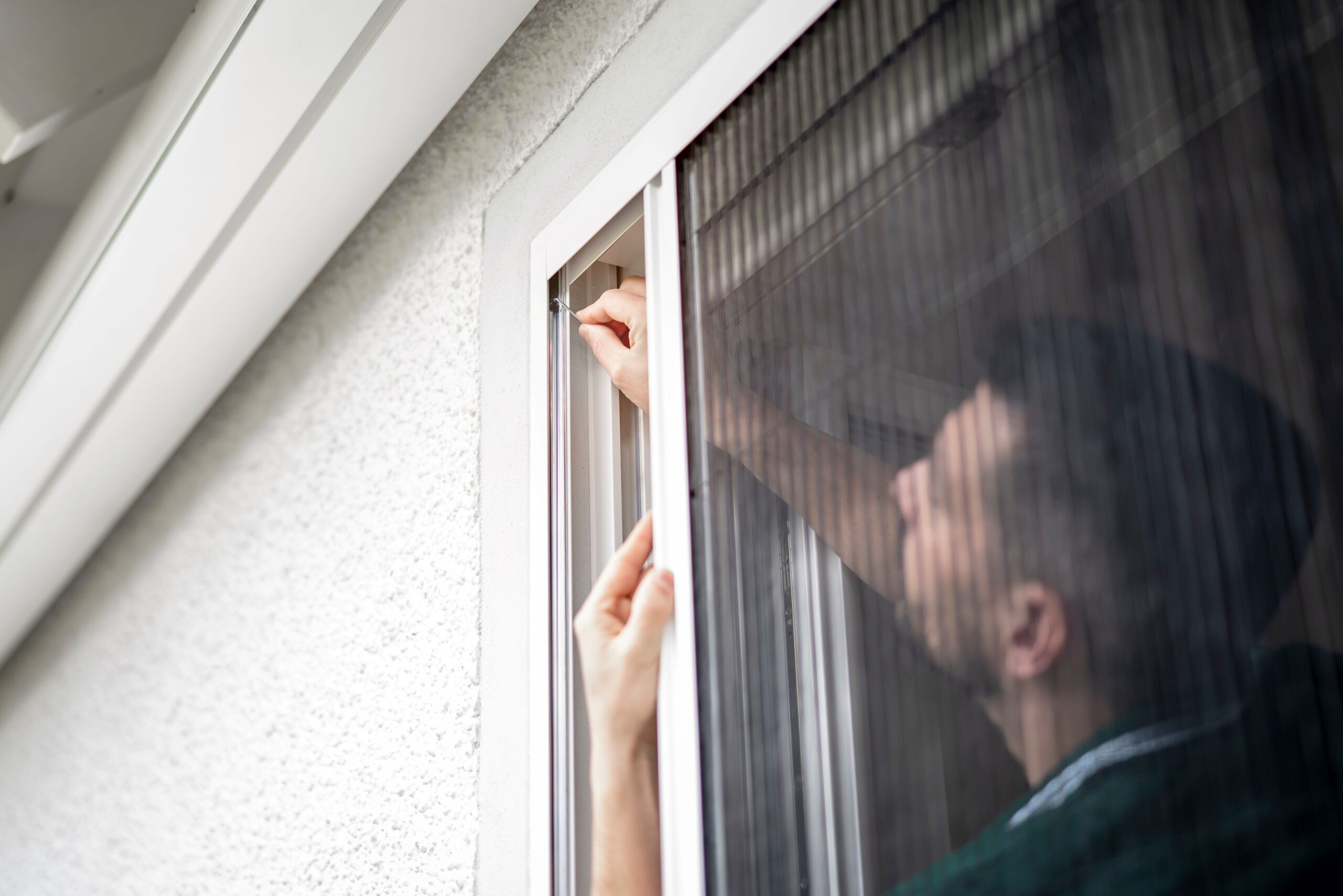 Eine Person installiert ein Fliegengitter an einem Fenster 